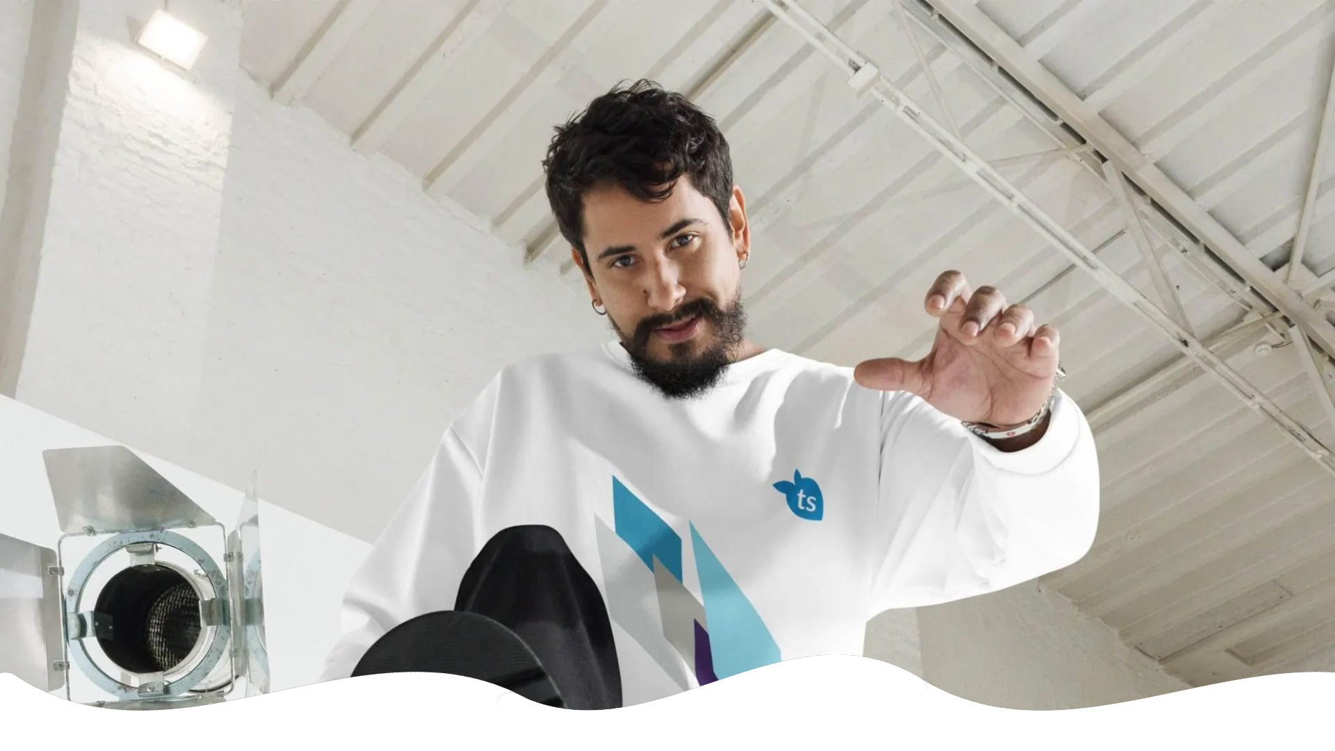 Man in a white sweatshirt with a logo, sitting on a white surface with a white ceiling in the background.
